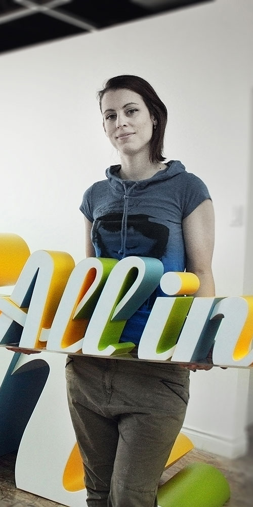 Woman holding a 3 dimensional logo prop reading All In