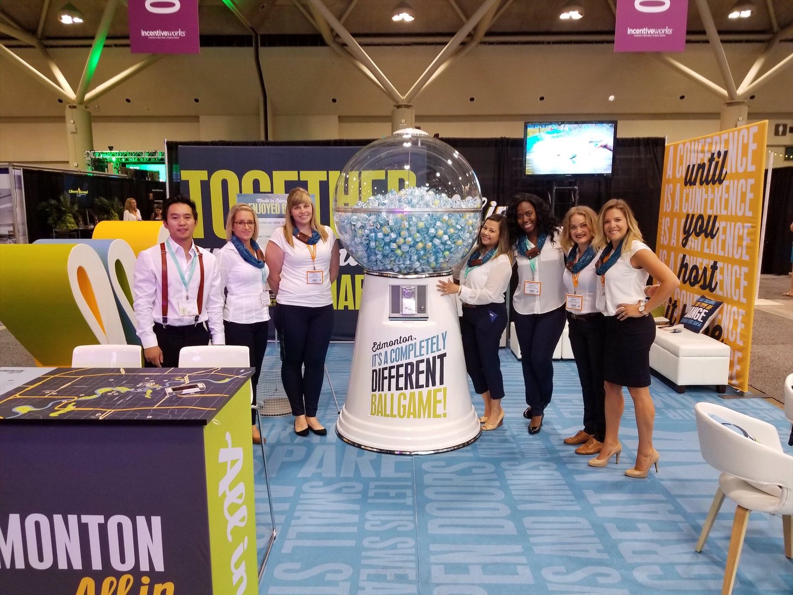 DQeZXNYVoAAAMDn Team of women presenting the Edmonton All In branded displays booth with a gum ball machine at a trade show.