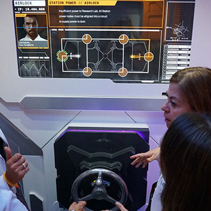 MovieProps_Bayer_Players_2 - The Bees Knees Design Scientists in front of a screen in a escape game, custom experiential.
