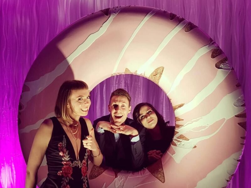 Stage props custom scenic fabrication of a giant donut sculpted photo op with 3 people posing inside and in-front of it..