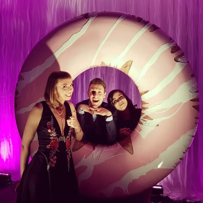 3 people posing inside and infront of a giant donut experiential photo booth. photo op fabrication.