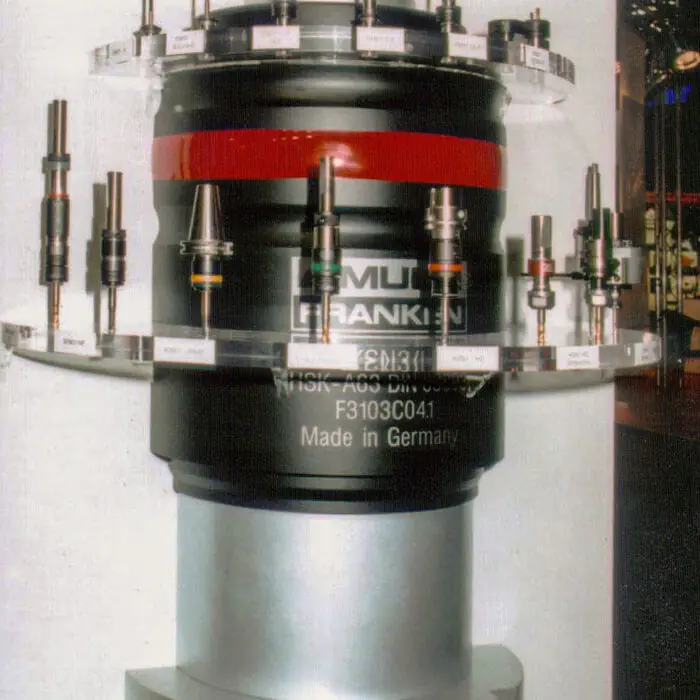 Industrial precision tool turret with multiple interchangeable bits arranged around a circular ring, labeled 'Franken' and 'Made in Germany' on a gray machine column, replica props.