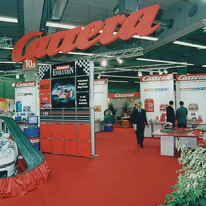 TradeShow_Carrera - The Bees Knees Design Indoor exhibition hall with Carrera race car booths, red carpet, large red Carrera sign, and promotional banners.
