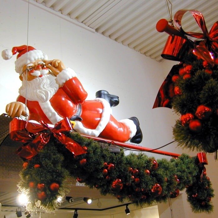 Santa Claus figure reclining on a red sleigh, adorned with festive red ribbons and green wreaths in a holiday display