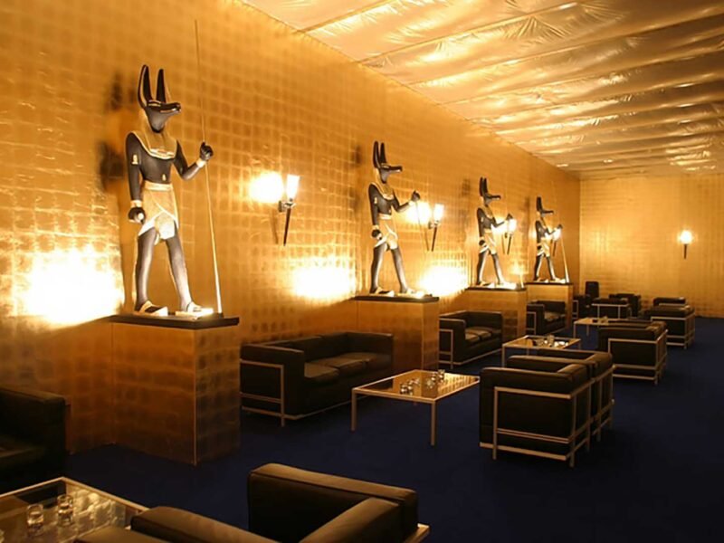 Gallery_Anubis_Exhibits Set of 4 Anubis museum sculptures in a row on raised pedestals in a golden cladded lobby.