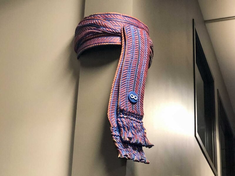 Gallery_Metis_Sash Colourful sculpture of a Metis Sash mounted on the corner of a wall.