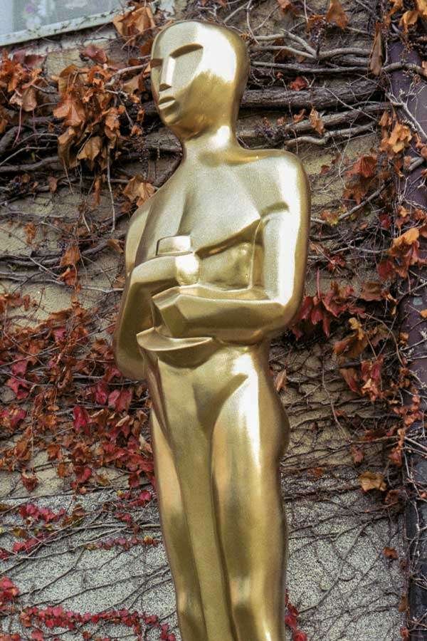 Oscar_Replica_1-4 7 feet tall Oscar statue replica finished in metallic gold set up in front of a plant wall.